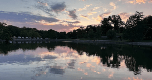 A serene lake at sunset, reflecting colorful clouds and trees along the shore.
