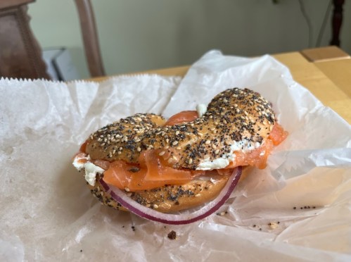 A bagel topped with smoked salmon, cream cheese, and red onion, resting on parchment paper.