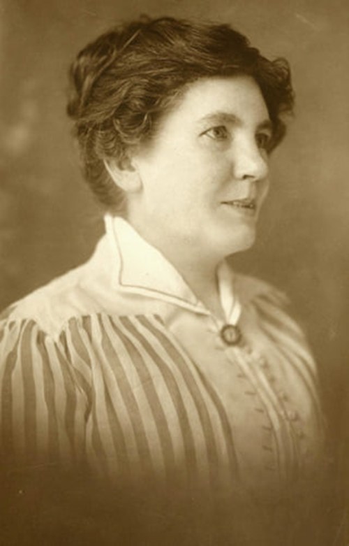 A sepia-toned portrait of a woman in a striped blouse, smiling softly, with her hair styled in loose waves.