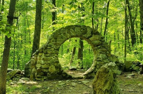 A stone archway surrounded by lush green trees in a serene forest setting.