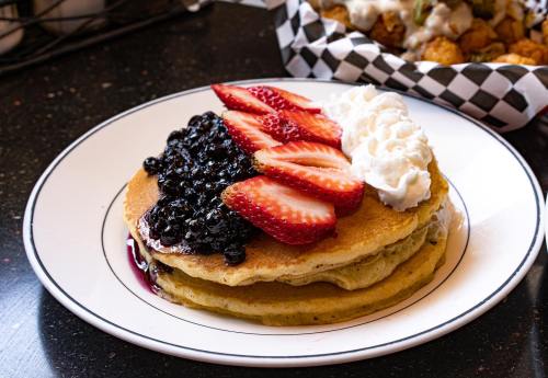 Stack of pancakes topped with strawberries, blueberries, and whipped cream on a black table.