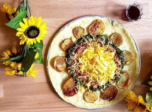 A colorful dish featuring a circular arrangement of greens, cheese, and crispy potatoes, surrounded by sunflowers.
