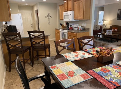 A cozy kitchen with wooden cabinets, a dining table set with colorful placemats, and bar stools at the counter.