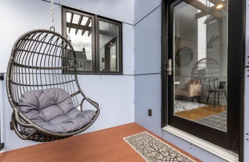 A cozy balcony featuring a hanging chair and a view of a stylish interior through a glass door.