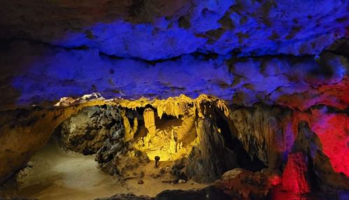 A colorful cave interior with illuminated stalactites and stalagmites in shades of blue, yellow, and red.