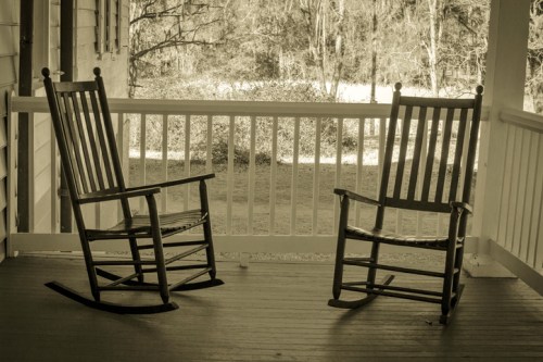 Two wooden rocking chairs on a porch, facing each other, with a blurred natural background.