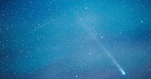 A comet streaks across a starry night sky, with a faint trail of light behind it.