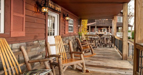 A rustic porch with wooden rocking chairs and tables, featuring a cozy cabin atmosphere.