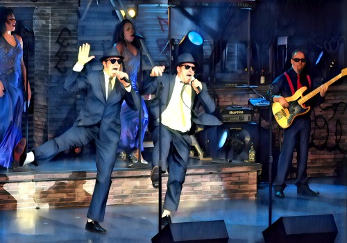 Two performers in suits and sunglasses dance energetically on stage, accompanied by a band and singers in the background.