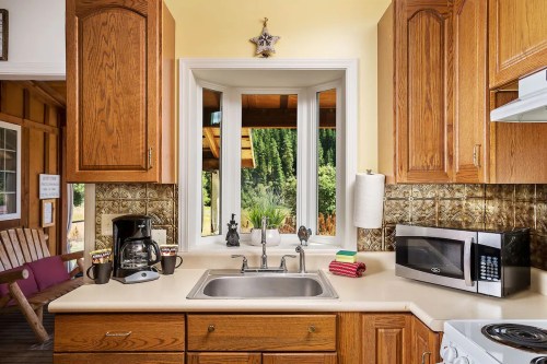 Cozy kitchen with wooden cabinets, a sink, coffee maker, and a view of greenery through a large window.