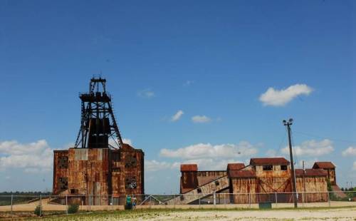 Rusty industrial building with a tall structure against a blue sky and scattered clouds.
