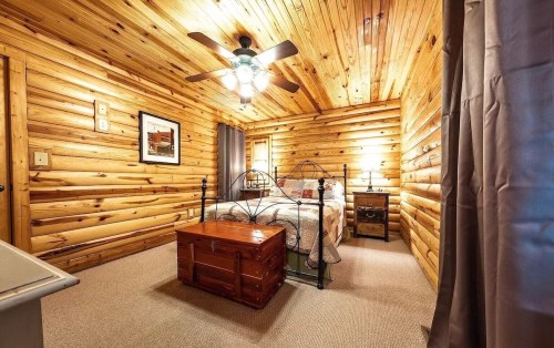 Cozy wooden bedroom with a bed, ceiling fan, and a wooden chest at the foot, featuring warm, rustic decor.