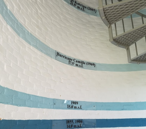 Interior wall with markings showing hurricane water levels, including Camille (1969) and Katrina (2005). Spiral staircase visible.