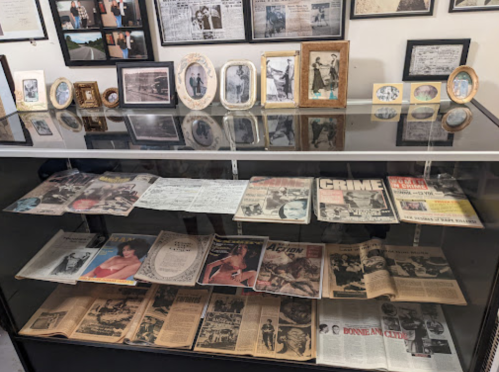 A display case filled with old newspapers, photographs, and framed pictures showcasing historical events and people.