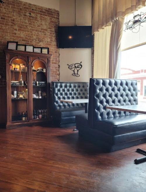 Cozy restaurant interior featuring leather booths, a wooden display cabinet, and large windows with natural light.