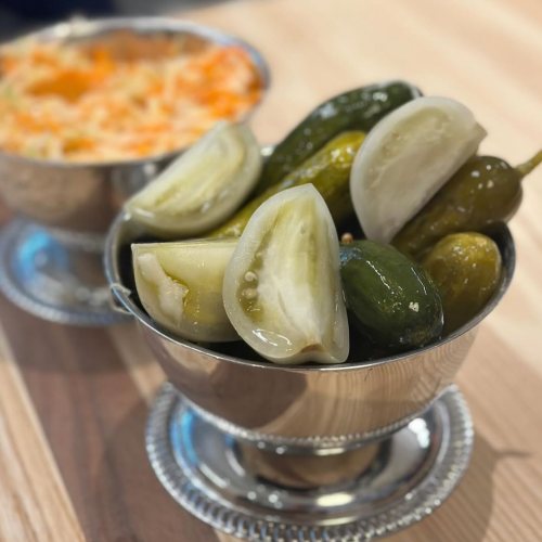 A silver bowl filled with assorted pickles, including green and yellow varieties, on a wooden table.