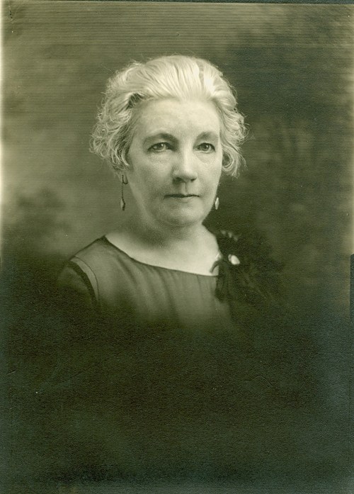 Black and white portrait of a woman with short, wavy hair, wearing a dress and earrings, looking directly at the camera.