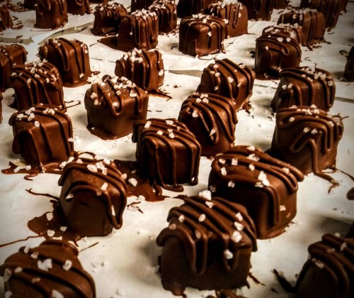 A close-up of chocolate-covered treats drizzled with chocolate and sprinkled with coarse salt on parchment paper.