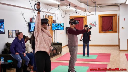 Two people are using VR headsets while others watch in a gaming room with colorful mats and screens.