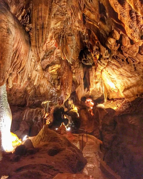 A dimly lit cave with intricate rock formations and illuminated pathways, showcasing natural textures and colors.