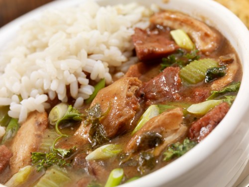 A bowl of savory stew with chicken, vegetables, and herbs, served alongside a portion of fluffy white rice.