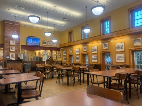 A spacious dining area with wooden tables, chairs, and framed photos on the walls, illuminated by overhead lights.