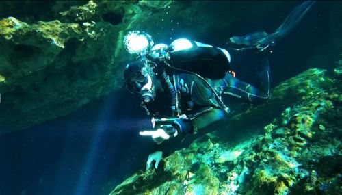 A diver explores an underwater cave, surrounded by rocks and bubbles, with light beams illuminating the scene.