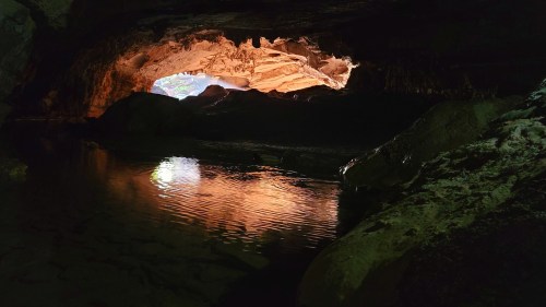 A dark cave with a glowing entrance, reflecting light on still water inside.