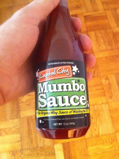 A hand holding a bottle of Capital City Mumbo Sauce, a 12 oz wing sauce from Washington, D.C.