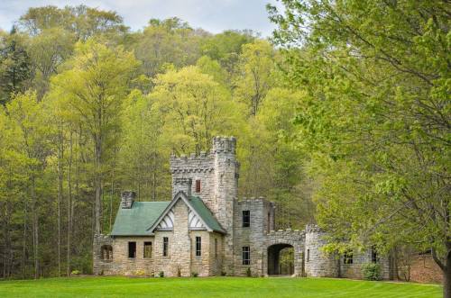 A stone castle surrounded by lush green trees and grass under a cloudy sky.
