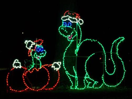 A festive dinosaur and a small character in a pumpkin, both outlined in colorful Christmas lights against a dark background.