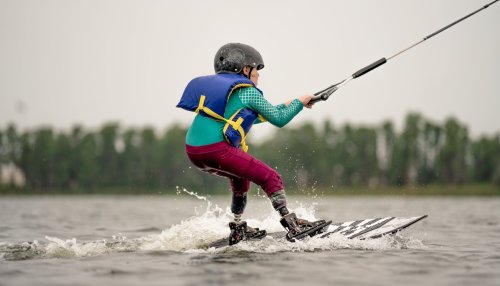A child with a helmet and life jacket water skiing on a lake, creating splashes behind them.