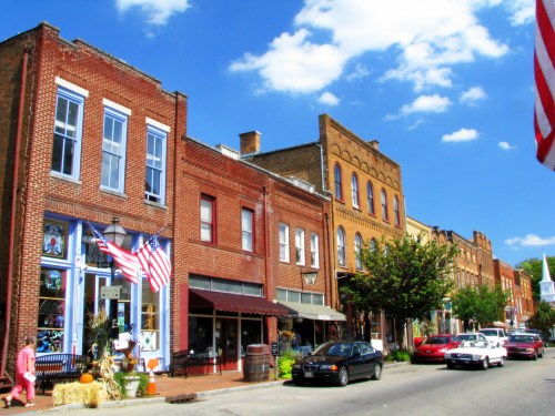 A charming street lined with brick buildings, shops, and American flags under a bright blue sky.