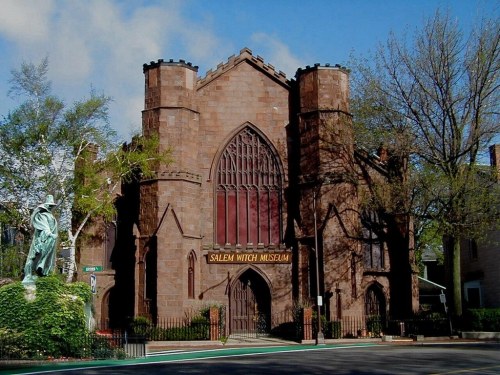 Historic Salem Witch Museum building with gothic architecture, surrounded by trees and a statue in the foreground.