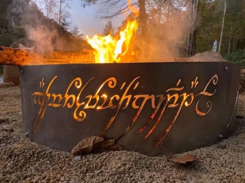 A fire pit with intricate metalwork featuring stylized, glowing script, surrounded by a natural outdoor setting.