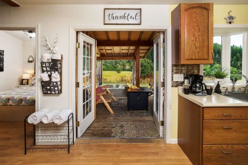 Cozy interior with open doors leading to a porch, featuring a kitchen area and a view of a green landscape outside.
