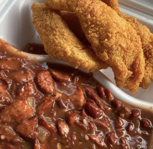 A close-up of a takeout container with fried fish and a side of red beans and sausage in a savory sauce.