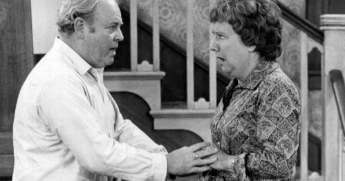 A tense black-and-white scene of a man and woman in a domestic setting, expressing strong emotions.