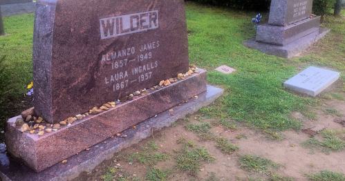 Gravestone of Almanzo James Wilder (1857-1949) and Laura Ingalls Wilder (1867-1957) in a cemetery, surrounded by flowers.