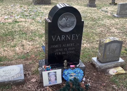 A black gravestone with the name "Varney" and dates, surrounded by flowers and a framed photo.