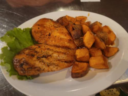 Grilled chicken breasts served with roasted sweet potatoes and a side of lettuce on a white plate.