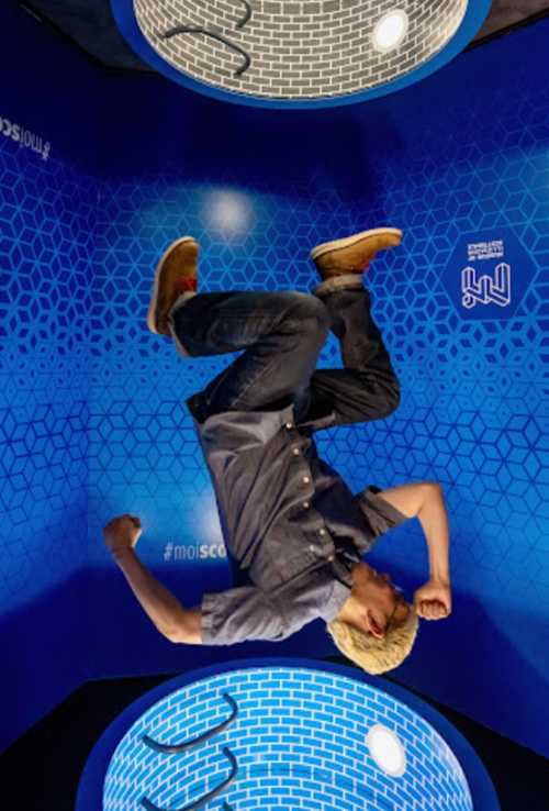 A person in a blue room appears to be upside down, striking a dynamic pose against a geometric background.