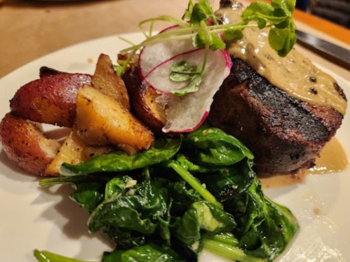 A plate featuring grilled meat with sauce, roasted potatoes, and sautéed spinach, garnished with radish and microgreens.