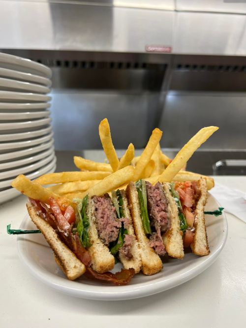 A plate with a stacked sandwich filled with lettuce, tomato, and meat, accompanied by crispy French fries.