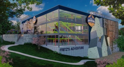 A modern adventure park building with climbing walls and colorful play structures, surrounded by greenery.
