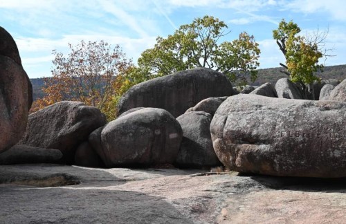 Large boulders scattered across a rocky landscape, with trees and a blue sky in the background.
