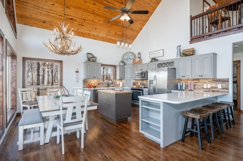 Modern kitchen with wooden accents, a large island, dining table, and high ceilings featuring a chandelier and antler decor.