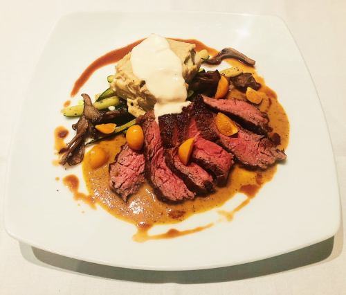 A gourmet plate featuring sliced beef, creamy sauce, vegetables, and garnishes on a white square dish.