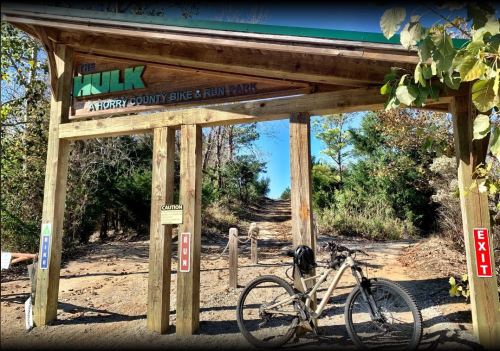 Entrance to The Hulk bike and run park in Horry County, featuring a wooden archway and a mountain bike.