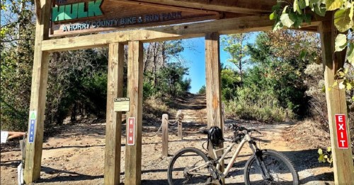 Entrance to Horry County Bike & Run Park, featuring a wooden sign and a bike parked at the trailhead.